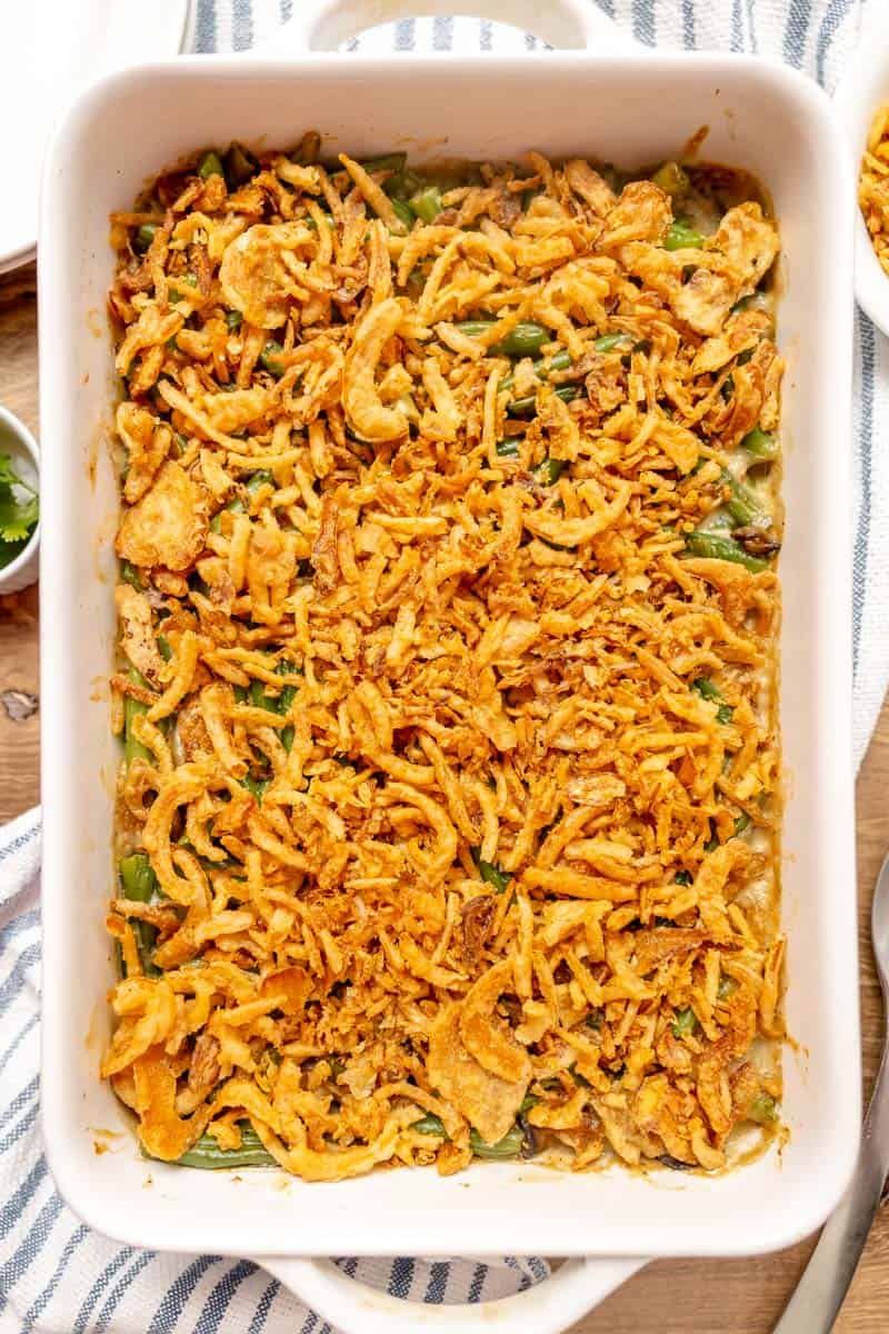 Baked green bean casserole topped with crispy fried onions in a white rectangular dish on a striped towel.