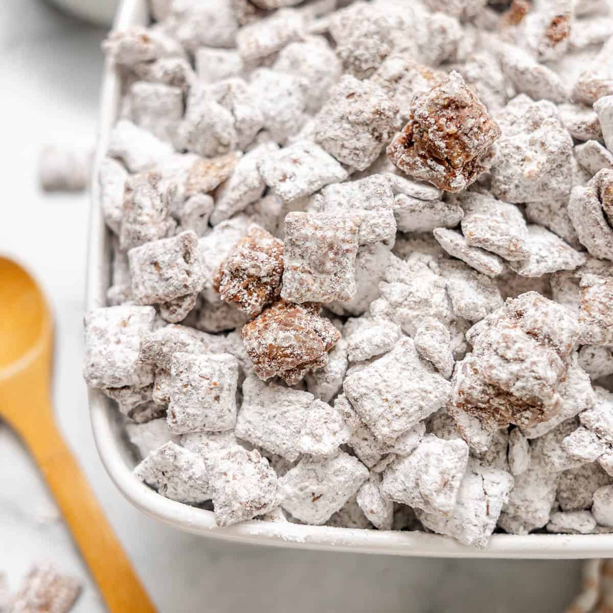 A close-up of a bowl filled with powdered sugar-coated cereal pieces, commonly known as puppy chow or muddy buddies.