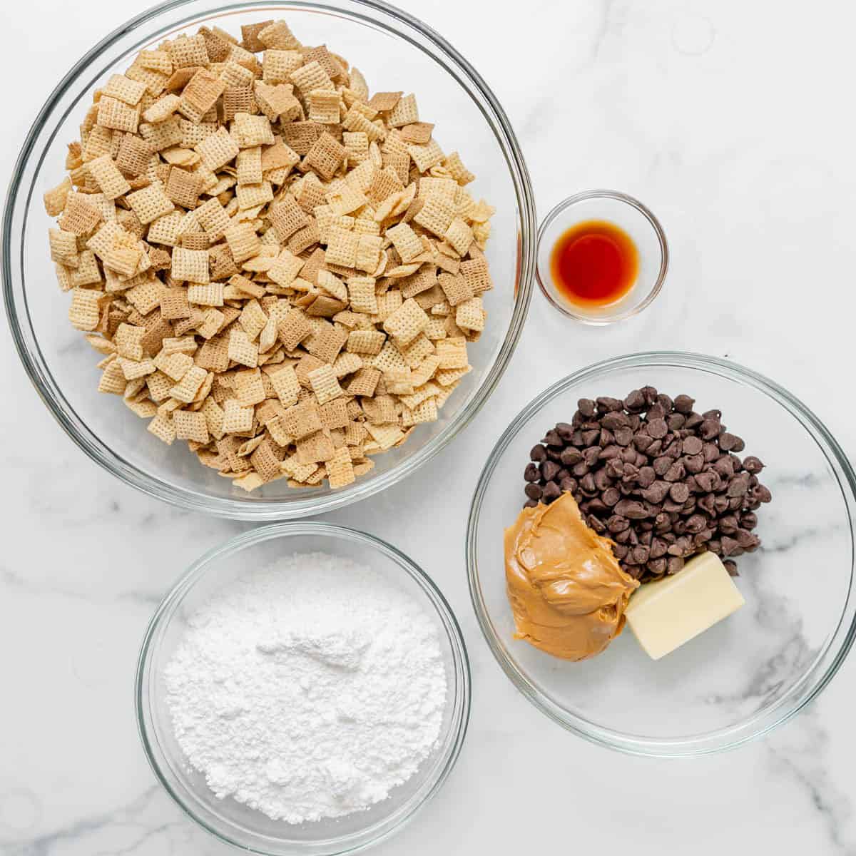 Four bowls contain Chex cereal, chocolate chips with butter and peanut butter, powdered sugar, and a small bowl of vanilla extract on a white surface.