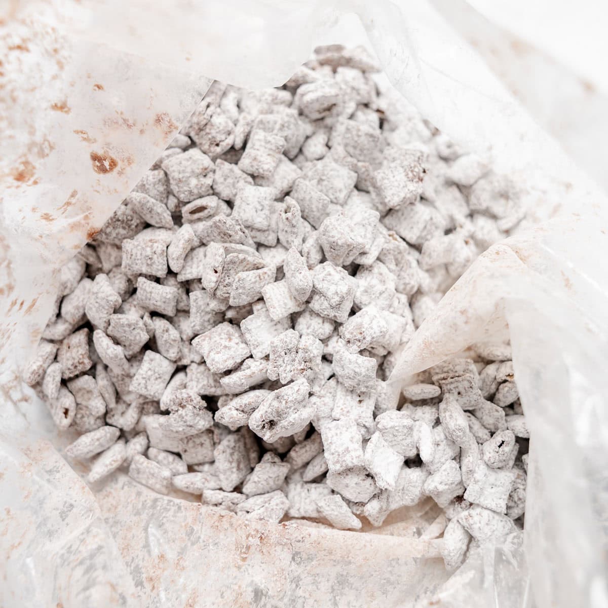 Close-up of a plastic bag filled with Chex cereal coated in powdered sugar, commonly known as puppy chow or muddy buddies.