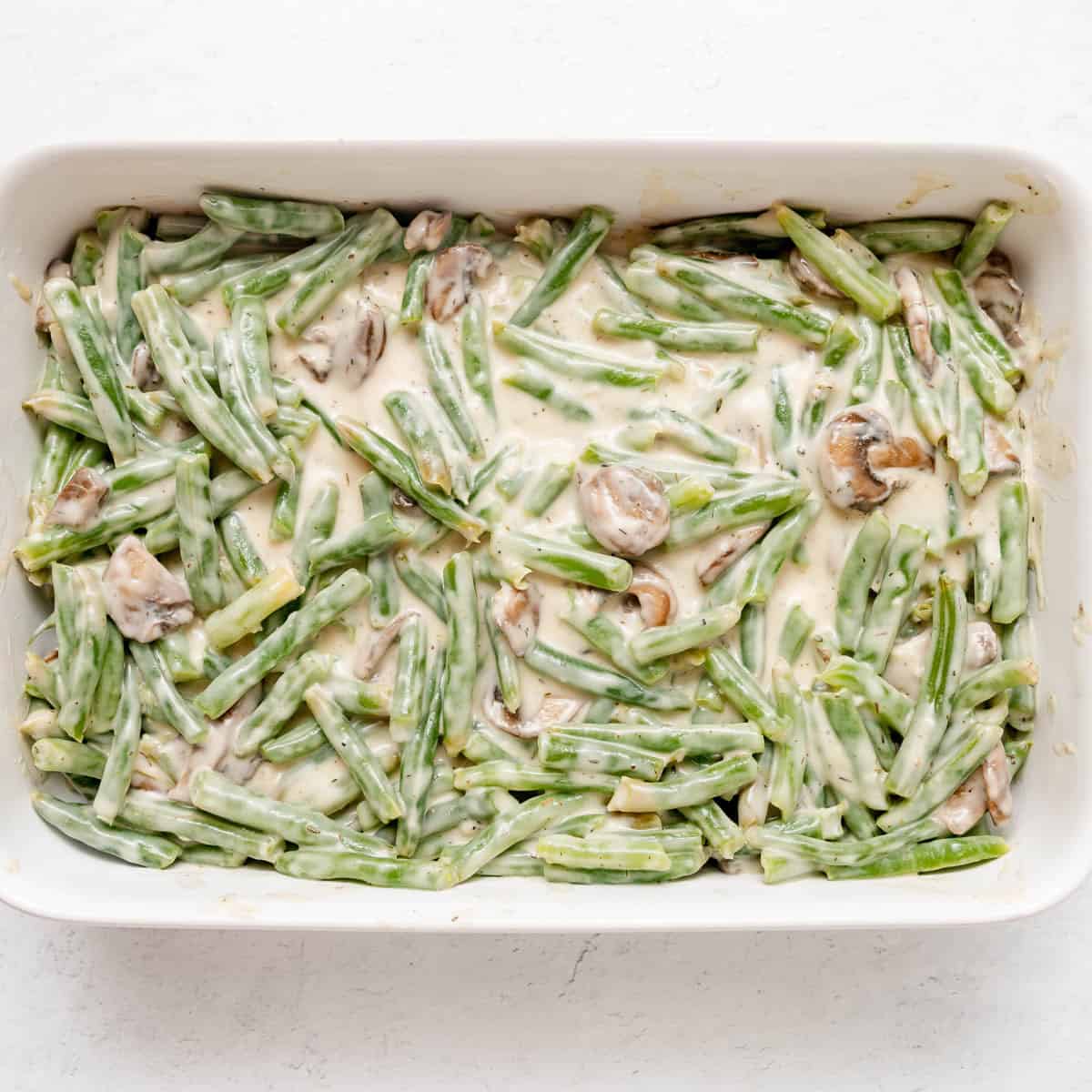 Casserole dish filled with green beans, mushrooms, and creamy sauce, uncooked and ready to be baked.