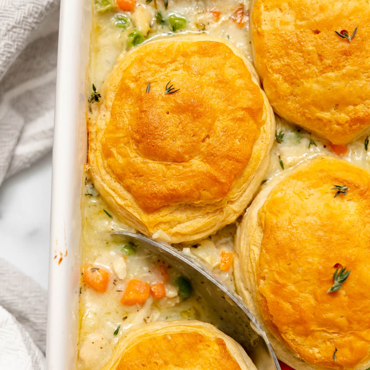 Chicken pot pie topped with three golden-brown biscuits in a white baking dish.