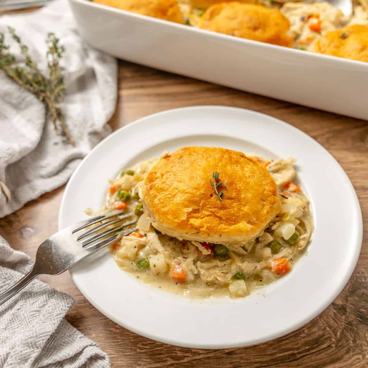 A plate of chicken pot pie with a single golden biscuit on top, accompanied by a fork.