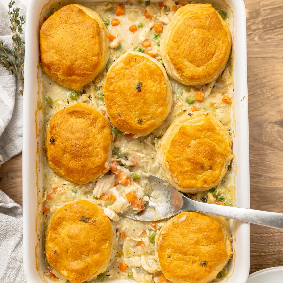 Chicken pot pie in a baking dish topped with six golden-brown biscuits, with a serving spoon resting in the center.
