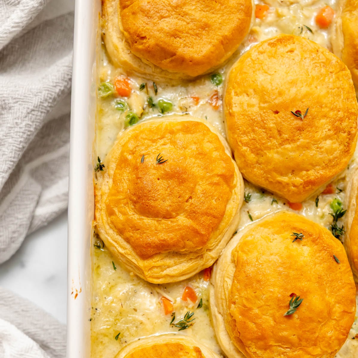 A rectangular baking dish filled with creamy chicken pot pie topped with golden-brown biscuits.