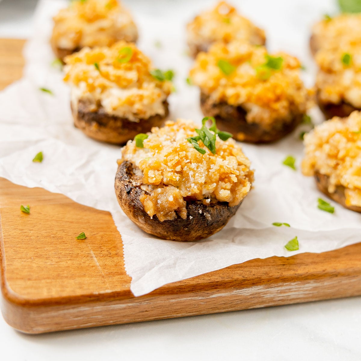 Stuffed mushrooms topped with breadcrumbs and green onions on a wooden board.