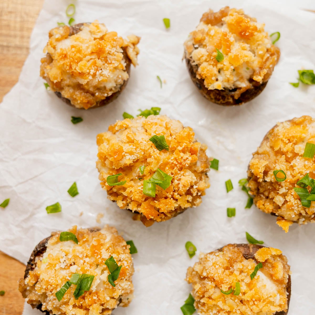 Six stuffed mushroom caps topped with breadcrumbs and chopped green onions on parchment paper.