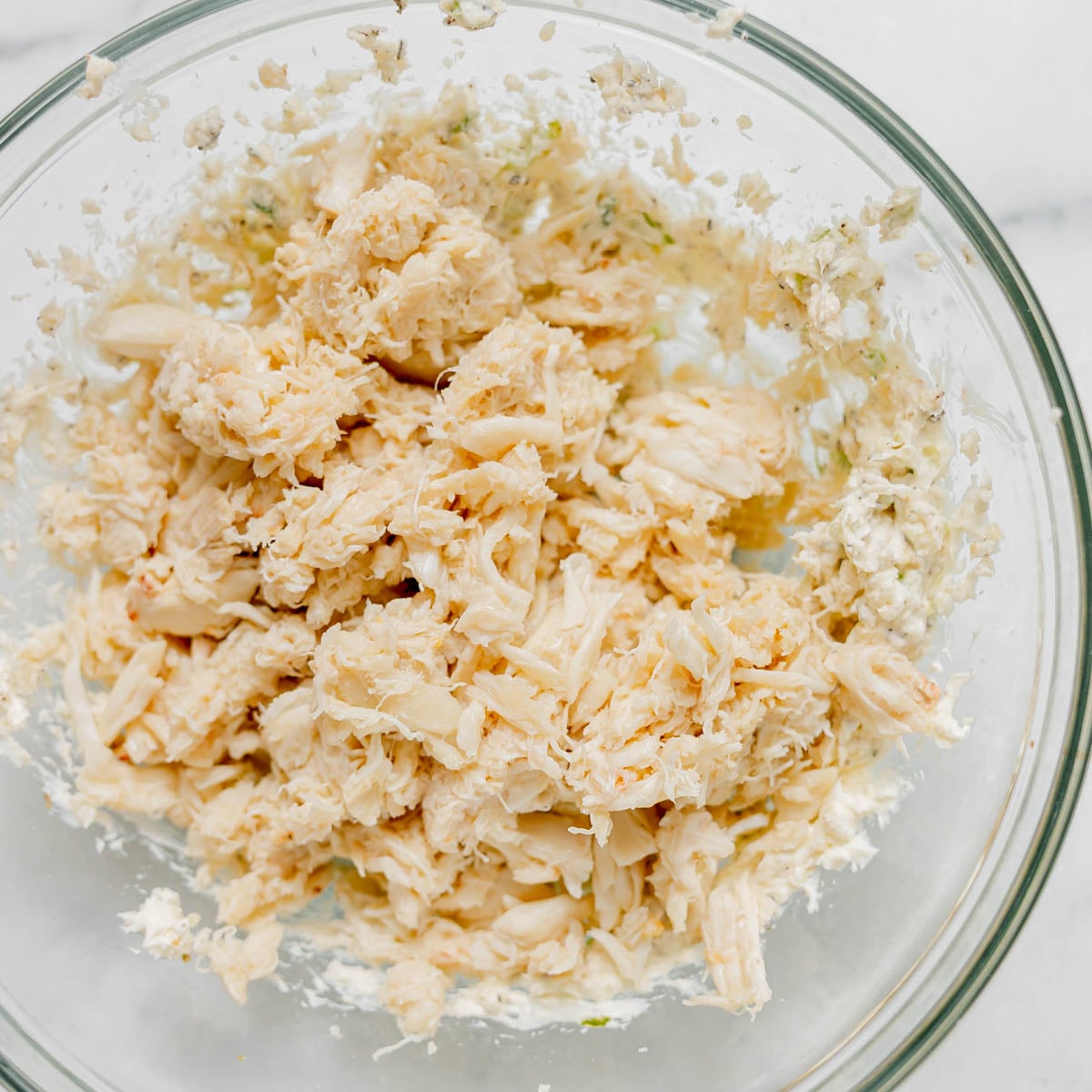 A glass bowl containing a mixture of flaked crab meat and creamy filling.