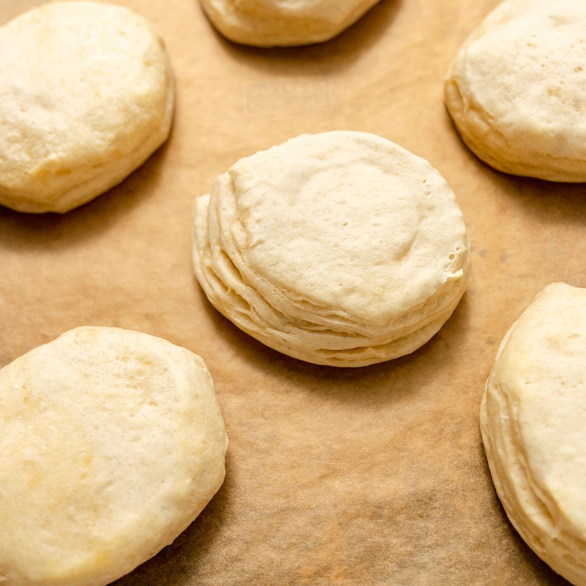 Six half baked biscuit dough rounds arranged on parchment paper.