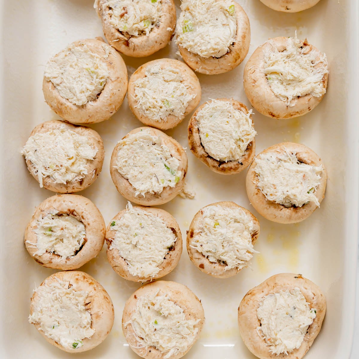 A baking dish filled with raw mushroom caps stuffed with a creamy crab filling.