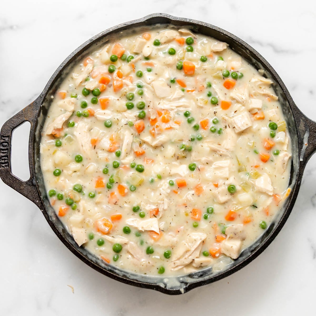 Cast iron skillet filled with creamy chicken pot pie filling featuring peas, carrots, and diced chicken.