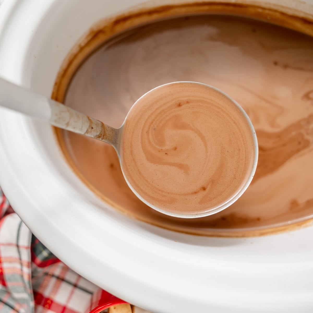 A ladle filled with hot cocoa being lifted from a slow cooker.