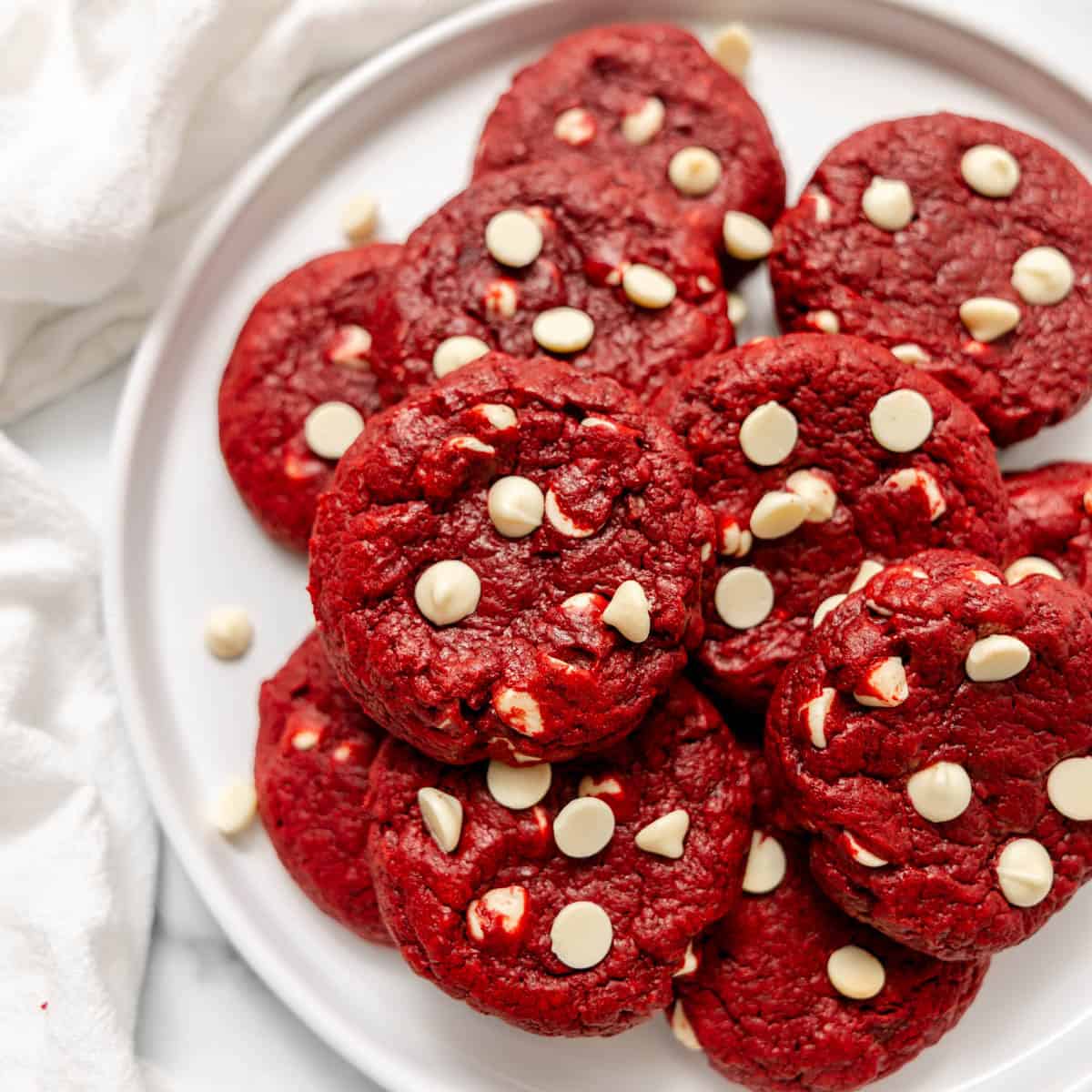 A pile of red velvet cookies studded with white chocolate chips on a white plate.