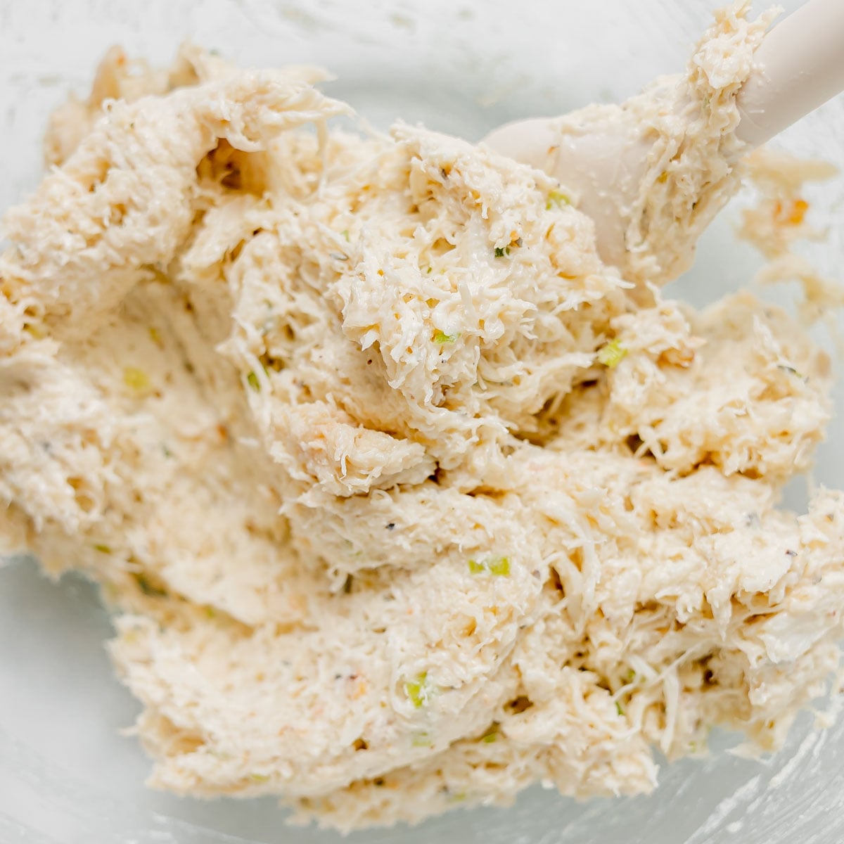 A spatula mixing a creamy crab cake mixture in a glass bowl.