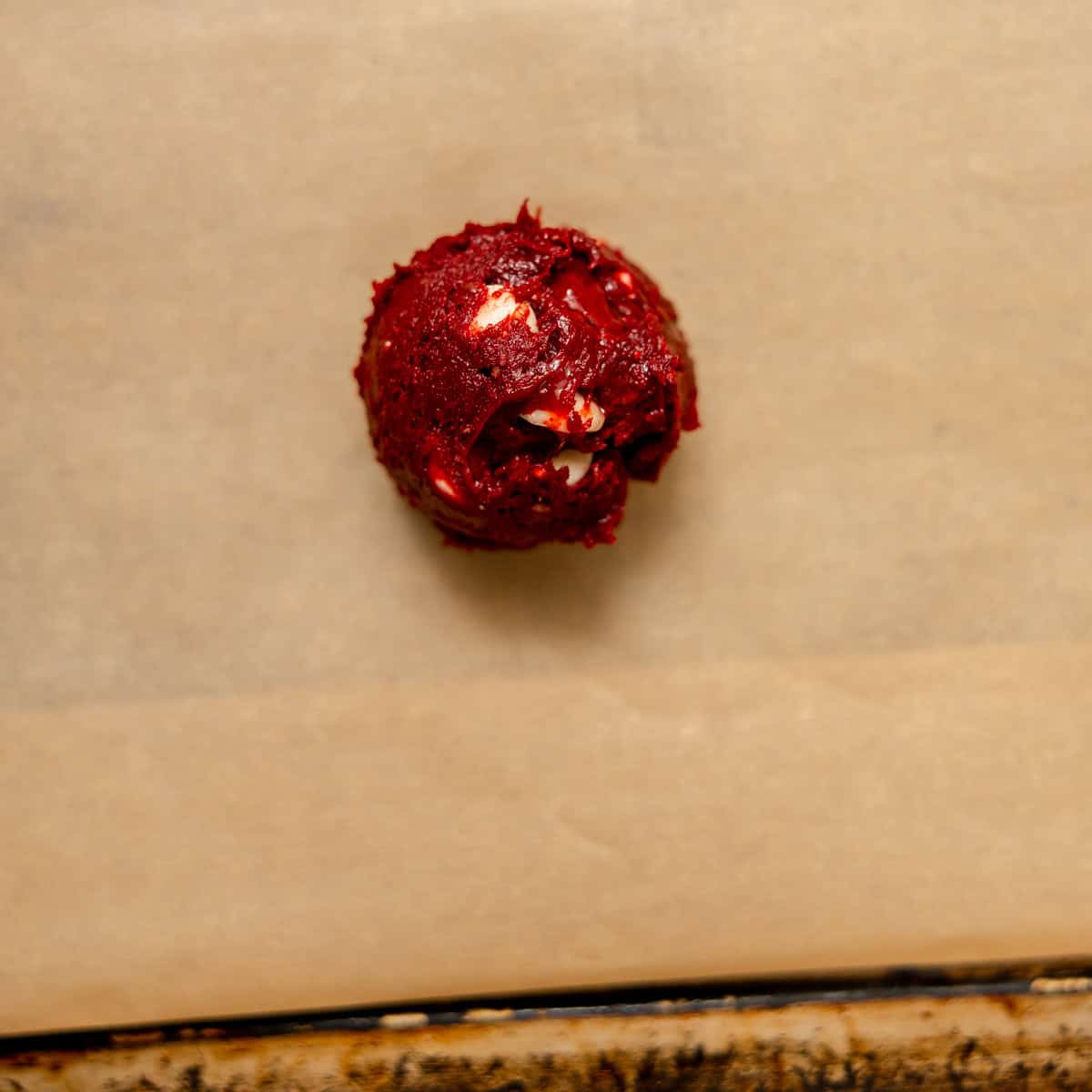 A scoop of red velvet cookie dough with white chips on parchment paper.
